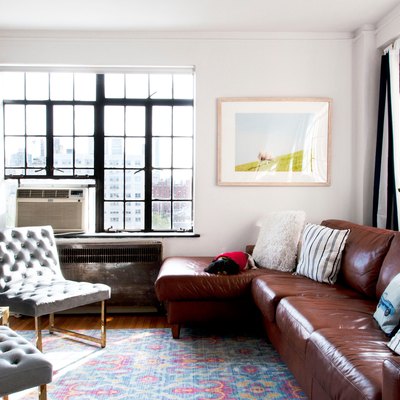 A living room is dominated by two gray upholstered chairs, a colorful pastel rug, and a leather sectional couch.