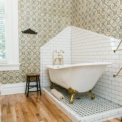 a claw-foot tub sits in a corner of a bathroom on a slightly  raised penny tile platform