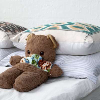 A brown teddy bear on a bed with white bedding and multicolored pillows