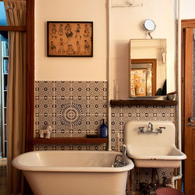 Rustic, old-fashioned style bathroom with white tub and sink, curtain, tiled walls, and wood door