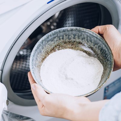 Hand holding bowl with white powder over white washing machine