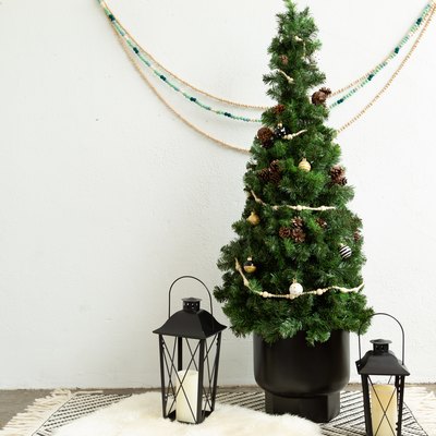 Small DIY Christmas tree with mini ornaments on black and white countertop placemat with lanterns against white wall with decorative hanging bead chains