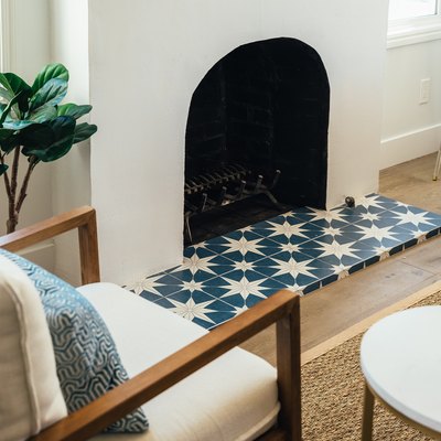 Blue and white star clay tile in front of fireplace. A tree houseplant, white cushioned accent chair, and round coffee table.