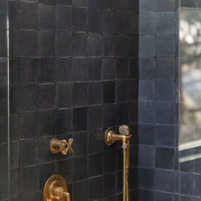 Shower with black and dark gray square wall tiles, and brass shower fixtures.