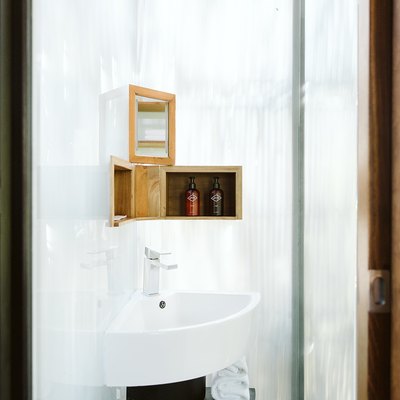 Small corner bathroom sink with small wooden shelves and bath products