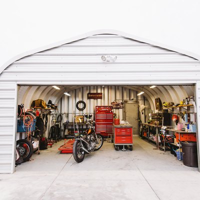 An open door workshop garage with a retro motorcycle, colorful storage cabinets, arched ceiling, and corrugated metal walls.