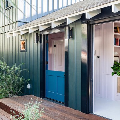 Exterior of a green and black home with a blue door, porthole windows, and open living room.