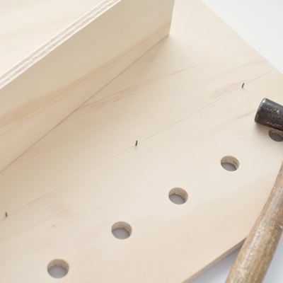 a hammer lies on a sheet of plywood with holes drilled in it and nails sticking through from the other side