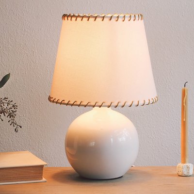 SKOTTORP lampshade with leather whipstitching, on a table with candlesticks, a book, and a vase of flowers