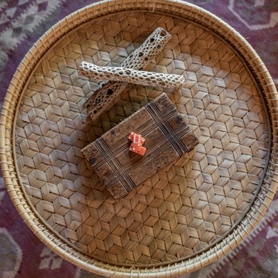 Round woven tray with a wood box and decorative sticks, on a purple and neutral rug.
