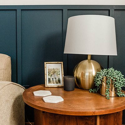 Blue board and batten wall, wood side table with a table lamp, and a beige accent chair