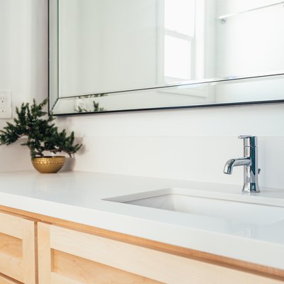 Light wood bathroom vanity with a white countertop, metal sink faucet, and a gold bowl with a plan clipping all underneath a mirror