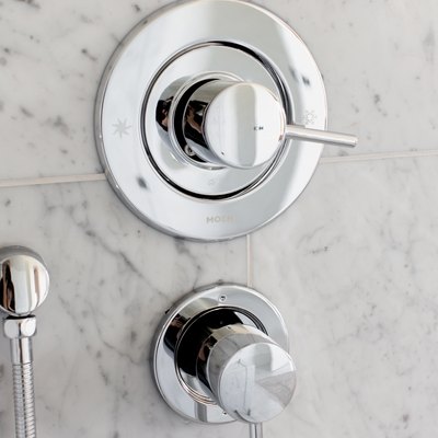 Silver shower faucets handles mounted on a granite or marble tile wall.