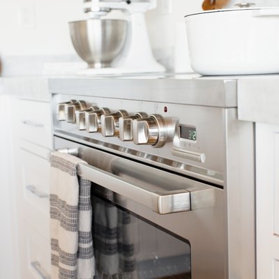 An oven door and temperature control knobs on a stainless steel range. A white and grey striped kitchen towel is hanging over the handle over the oven door.