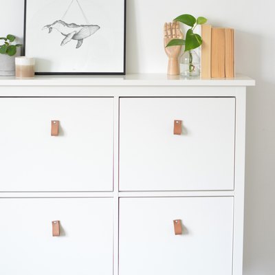 White dresser with leather pull handles on drawers with art and plants