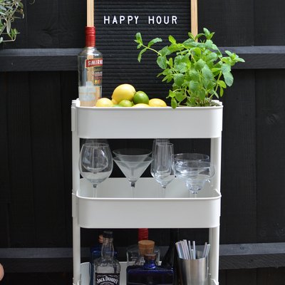 White bar cart with liquor bottles, glasses, and plant