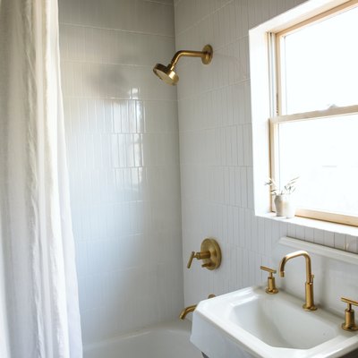 industrial farmhouse white sink with a gold faucet and white tiles in a bathroom