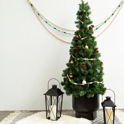 Small DIY Christmas tree with mini ornaments on black and white placemat on countertop with lanterns against white wall with decorative hanging bead chains