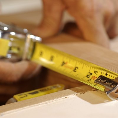 Close-up of man's hands as he measures a piece of wood.