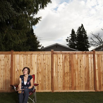 Woman sitting on chair in lawn by wooden fence
