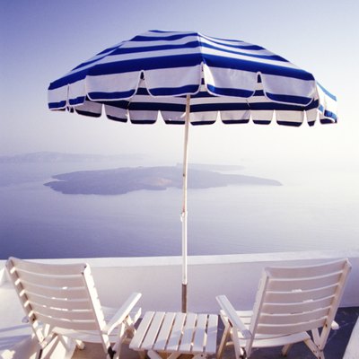 Rear view of wooden chairs and a table with umbrella on a balcony overlooking the ocean and the Greek Isles.
