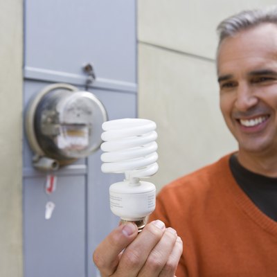 Man with home electric meter and compact fluorescent light bulb