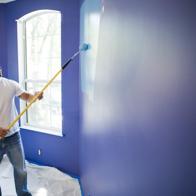 Young man painting wall with paint roller in house
