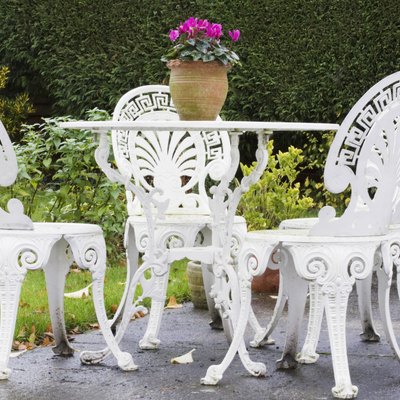 White-painted, decorative garden furniture on patio, including four chairs and plant in terra cotta pot in center of table