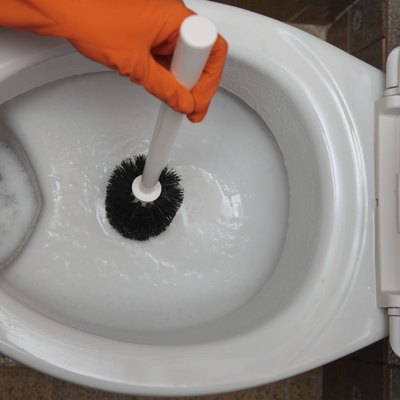 Gloved hand cleaning toilet bowl using brush