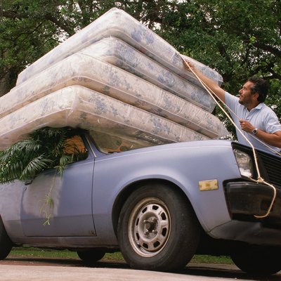 Man fastening four mattresses to roof of car