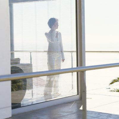 mid adult woman standing behind blinds and talking on a mobile phone