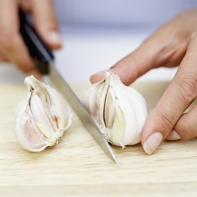 Woman's hands chopping garlic with a knife on a wooden board