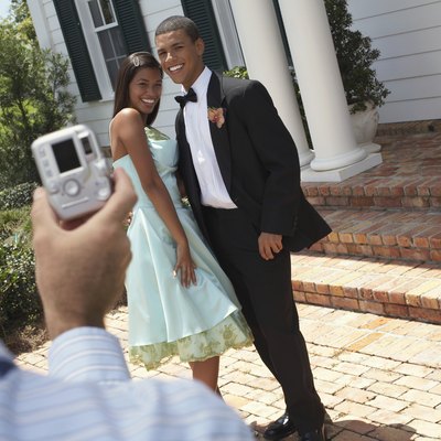 Man photographing young couple wearing evening dress, outdoors,smiling