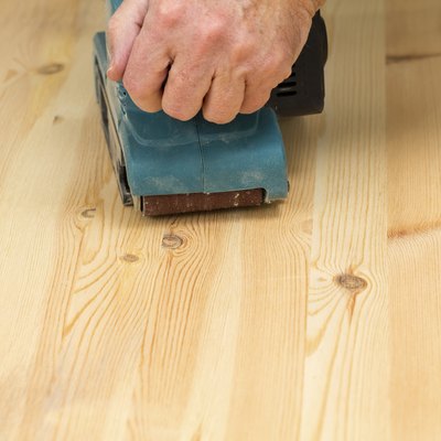 Mans hand on belt sander with pine wood