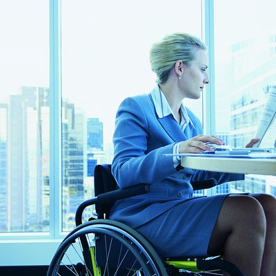 Businesswoman Sitting in a Wheelchair Working on a Laptop in the Office
