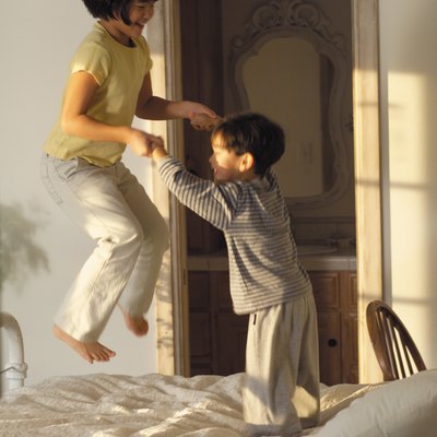 lifestyle photograph of two asian children as they play together and jump on the bed