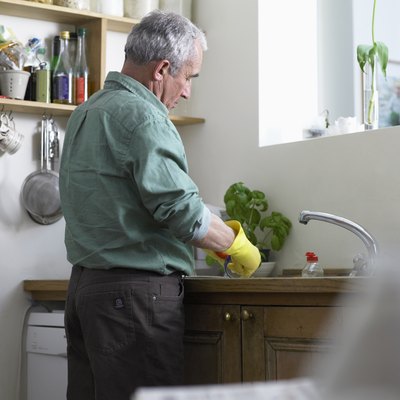 Senior man wearing rubber gloves washing up at sink (focus on man)