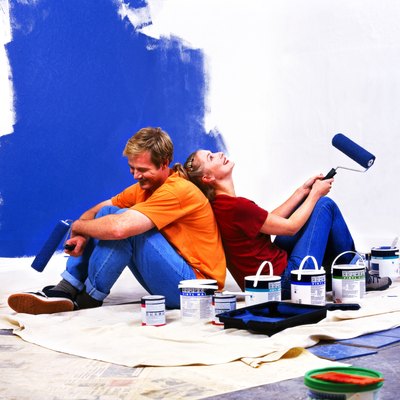 side profile of a couple sitting back to back with roller brushes of paint in hand