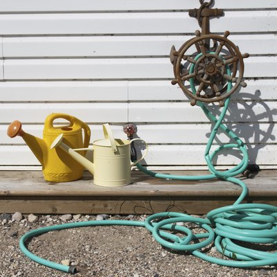 Green water hose and two watering cans outdoors