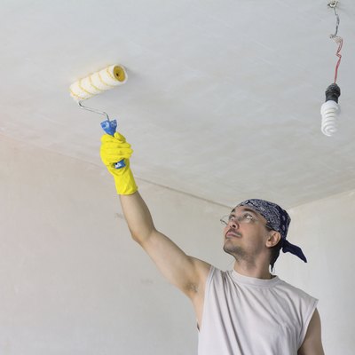 Young worker painting ceiling with roller