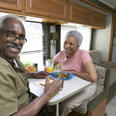 Senior Couple Sit at a Table in a Motor Home, Having Lunch