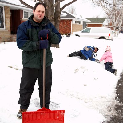Father posing with snow shovel while children play
