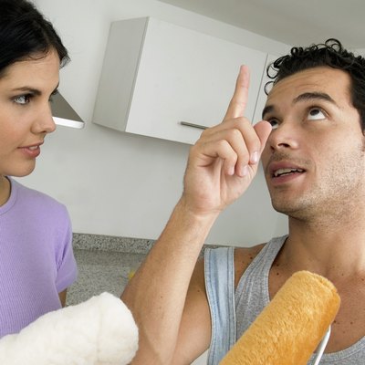 Couple holding paint rollers, with main pointing at ceiling, close-up