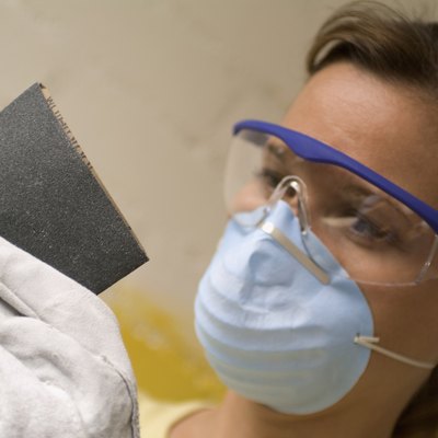 Close-up of a woman holding sand paper wearing a dust mask and safety goggles