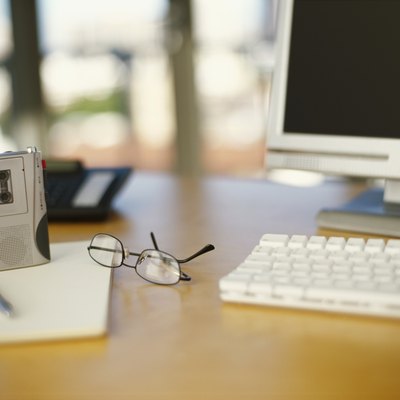 close-up of a computer with a personal cassette player and eyeglasses on a table
