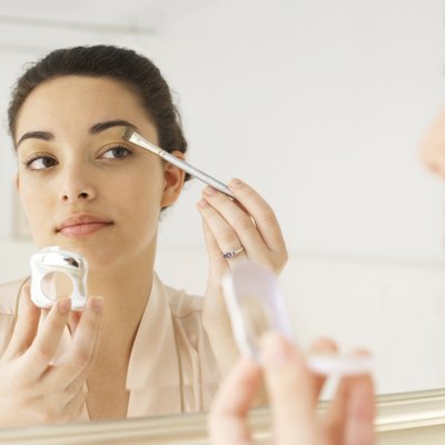 Young woman applying make-up in mirror, using brush, close-up