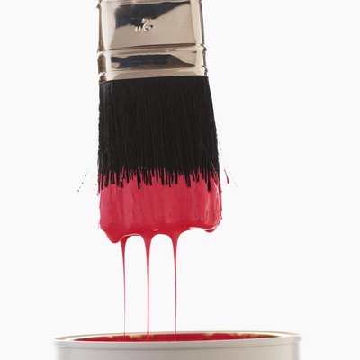 Paintbrush dripping red paint into paint can, close-up