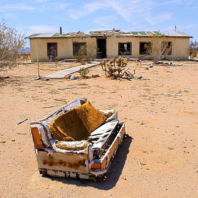A torn up couch sits outside in front of a dilapidated building.