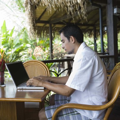 Man working on laptop computer in tropical cafe