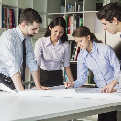 Four architects standing and planning around a table while looking down at blueprint
